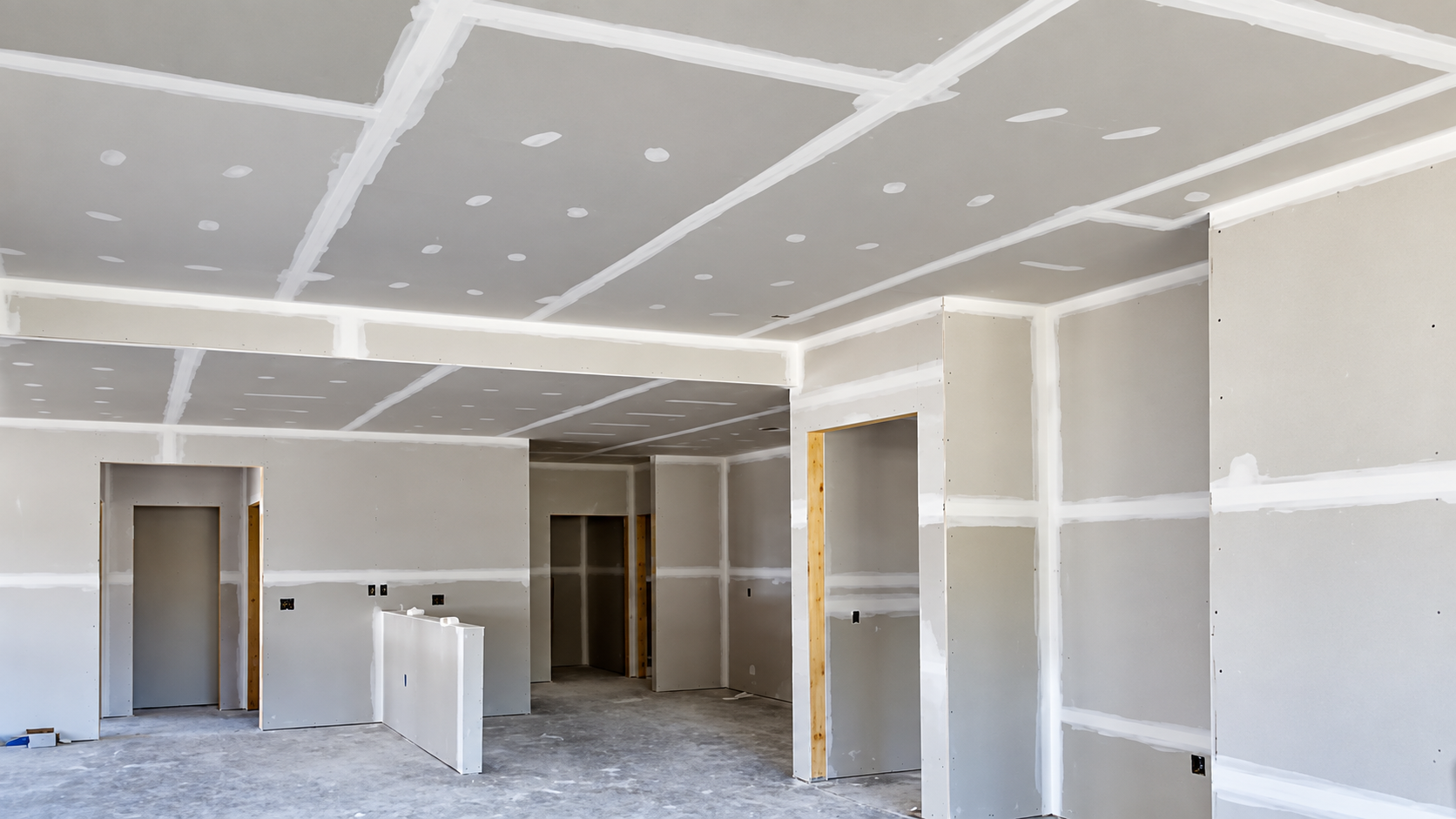 Freshly hung drywall on the walls and ceiling, with taped and mudded seams and open doorways, in a home under renovation
