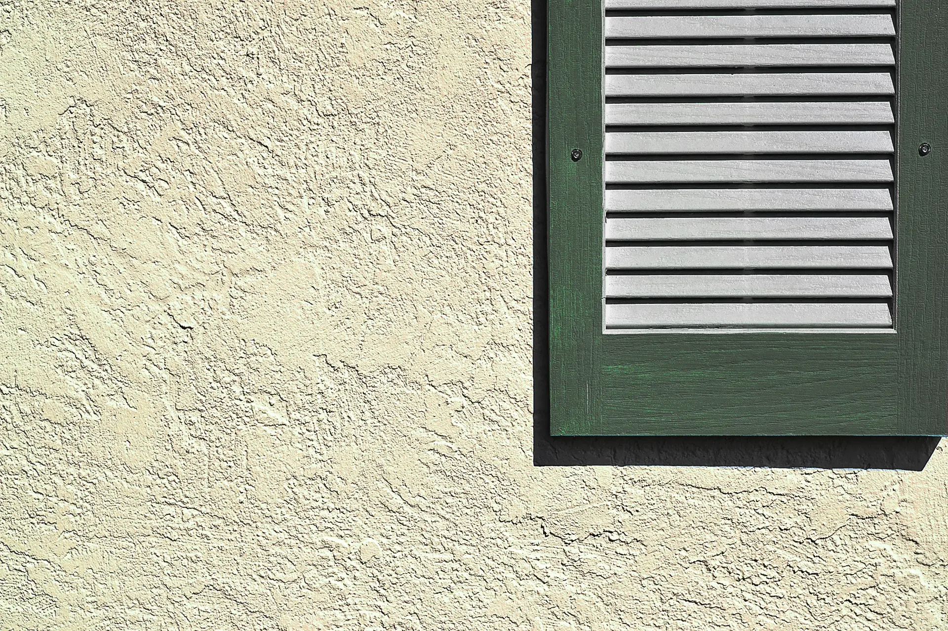 Textured stucco wall beside a green louvered gable vent