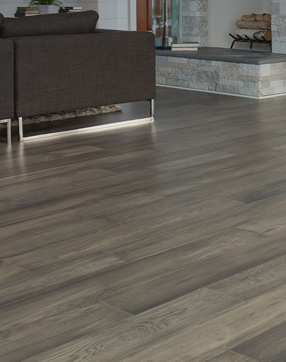 Living room with wide-plank grey-brown flooring, a dark sofa with chrome legs, and a stacked-stone fireplace hearth